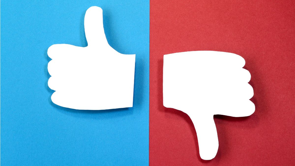 Auf bunter Pappe direkt nebeneinander zwei aus Papier ausgeschnittene Daumen. Ein Daumen hoch, einer runter