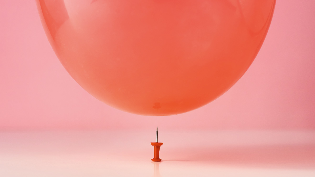 Luftballon, der über einer mit der Spitze nach oben stehenden Stecknadel schwebt.