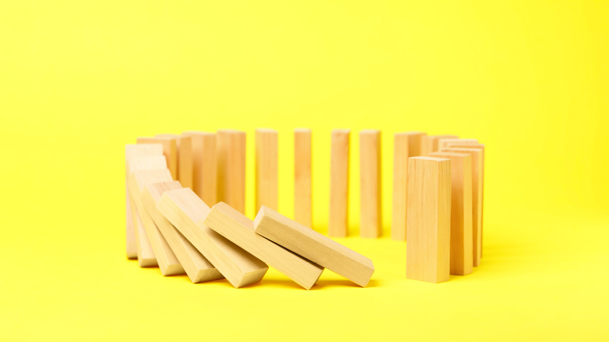 Im Kreis aufgestellte Domino-Steine, die begonnen haben, umzufallen. Gelber Hintergrund.