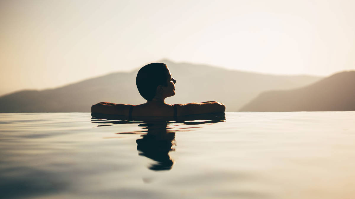 Silhouette einer Frau in einem Pool, die verträumt in die Landschaft schaut