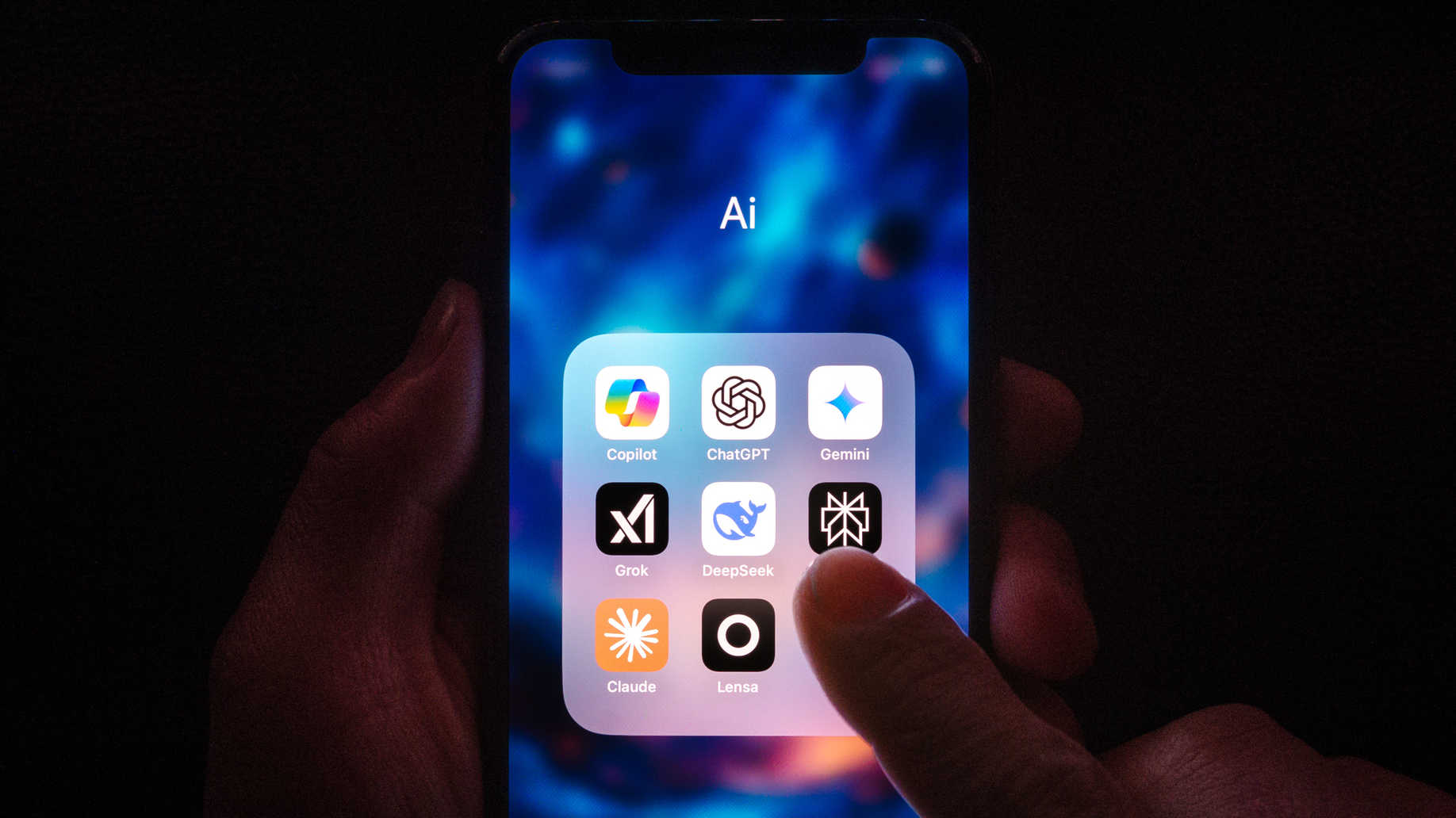 Eine Person hält ein Handy, darauf zu sehen sind mehrere Apps von gängigen KI-Chatbots