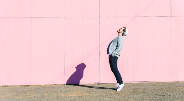 Fröhlicher Mann in Tanz-Pose im Profil vor pinkfarbener Wand.