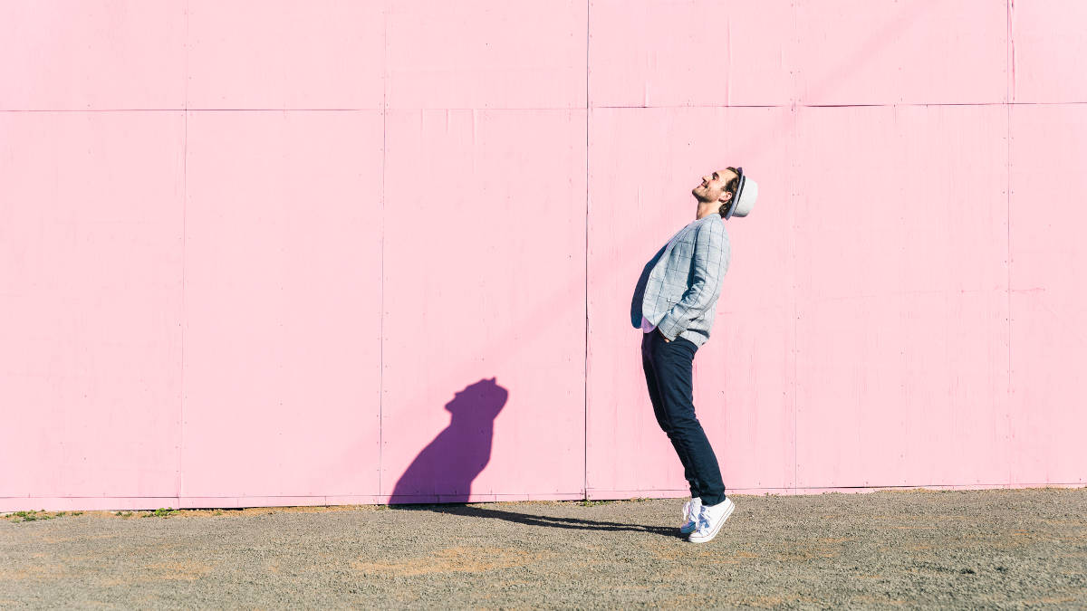 Fröhlicher Mann in Tanz-Pose im Profil vor pinkfarbener Wand.