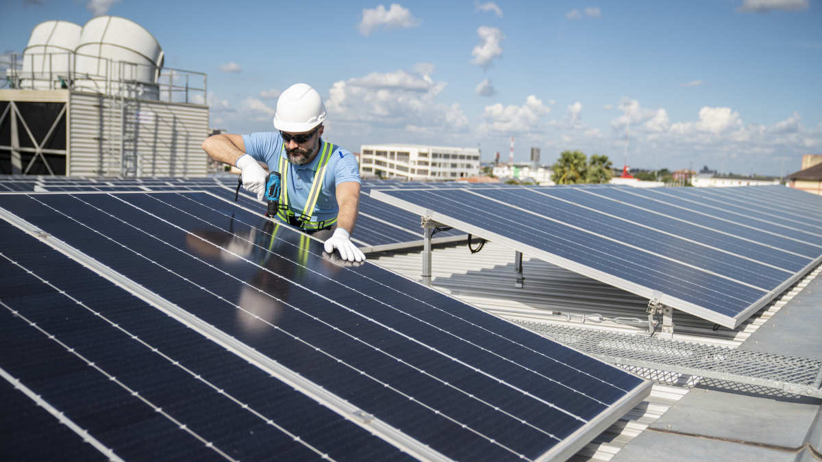 Mensch installiert Solaranlage auf Dach.